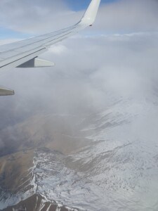 A photo of an airplanes wing. There are clouds in the sky and a view of snow capped mountains below.