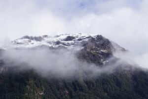 A snow caped mountain shrouded in cloud.