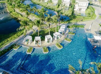 Aerial view of swimming pool area with slides, water play structures, umbrellas, and palm trees.