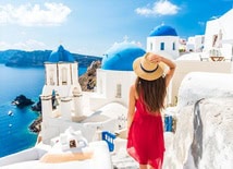 Woman in flowing red dress overlooking whitewashed houses and blue domes in Santorini, Greece
