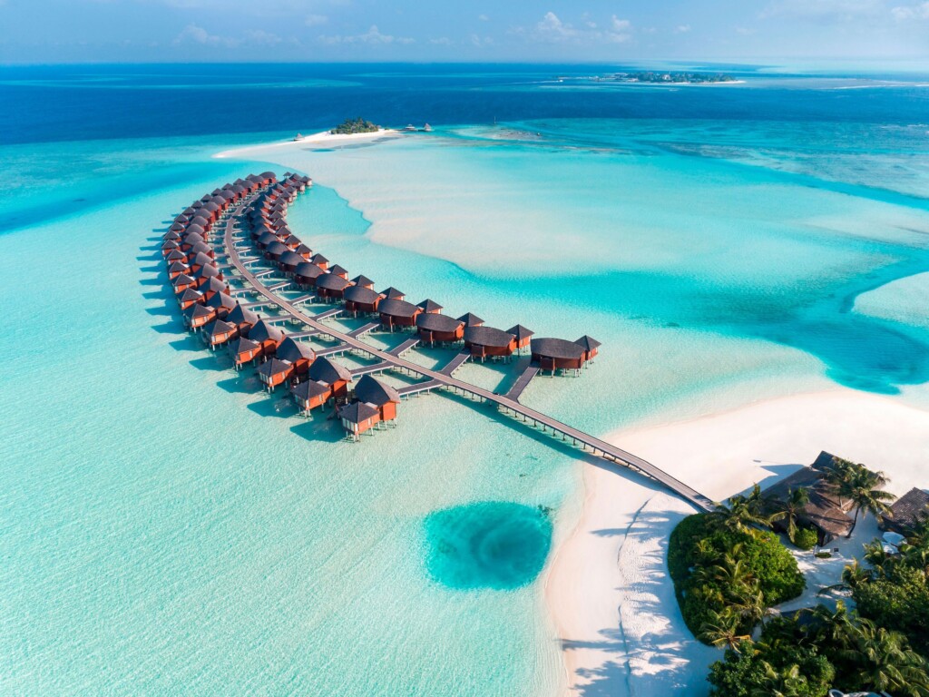 A photo taken from above of overwater bunglows in the Maldives with sandy-aqua water surrounding