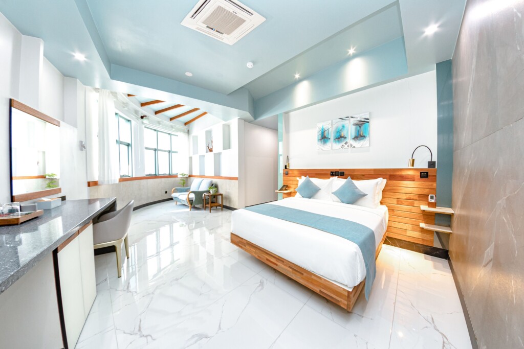 Inside view of a Deluxe Room at Marukab Plaza in Male. a large fresh double bed within a spacious room with a wall of windows