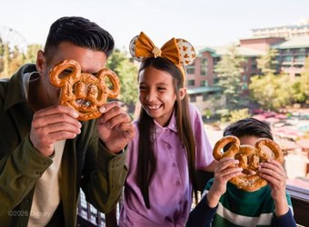 Two kids with a dad in Disneyland holding Mickey Mouse shaped pretzels